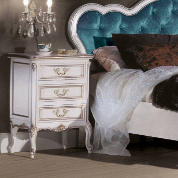 Comodino 3 cassetti con particolari intagliati vicino a letto